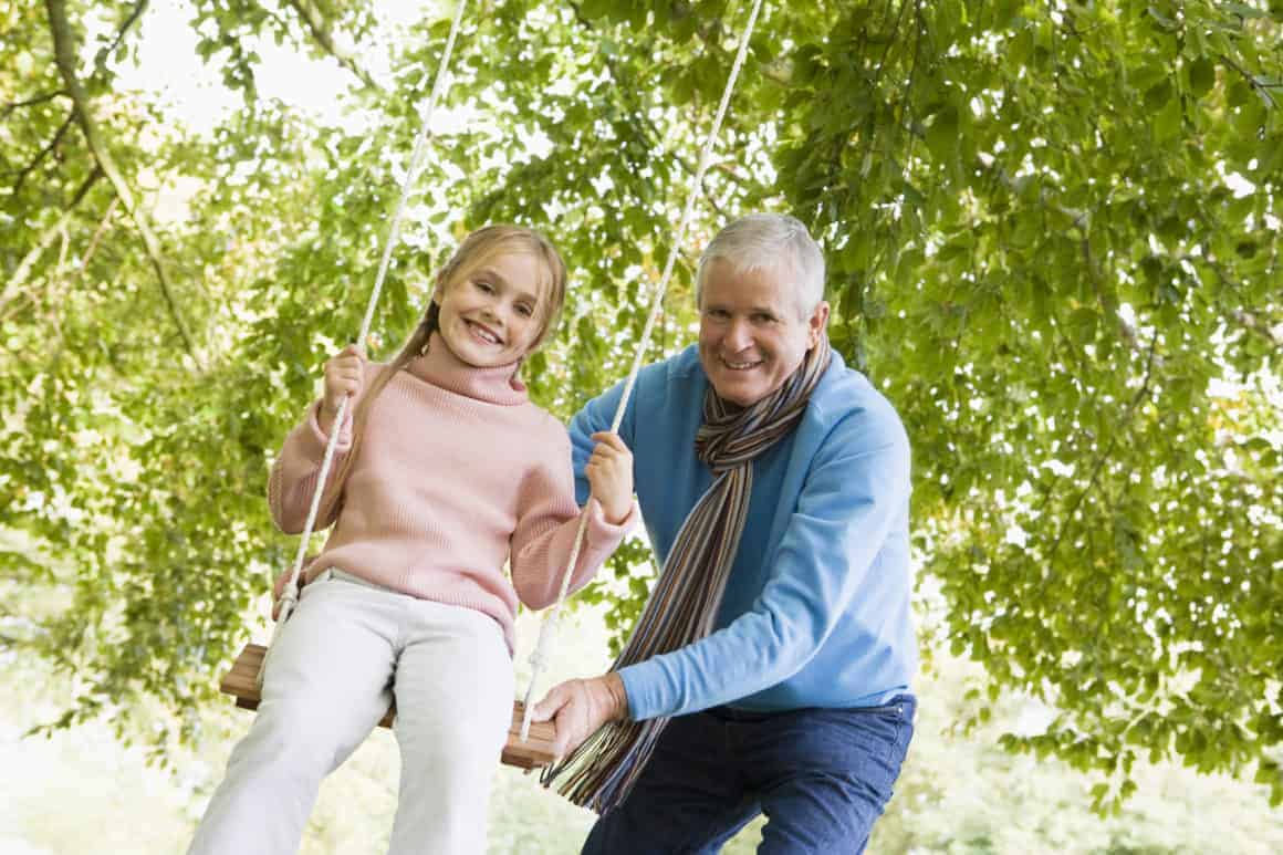 grandfather-pushing-granddaughter-on-swing-and-smiling