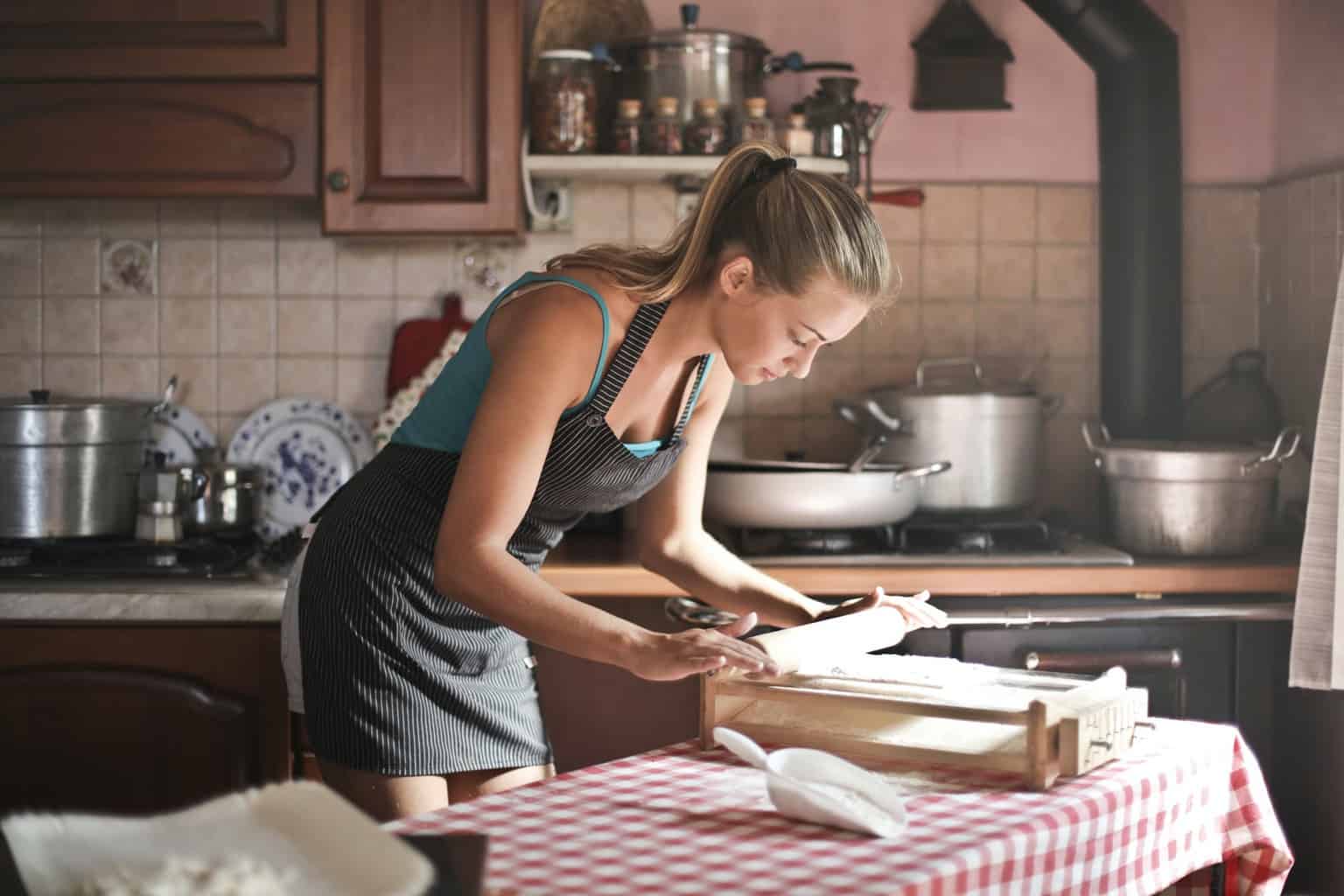 young woman rolling dough for baking in kitchen