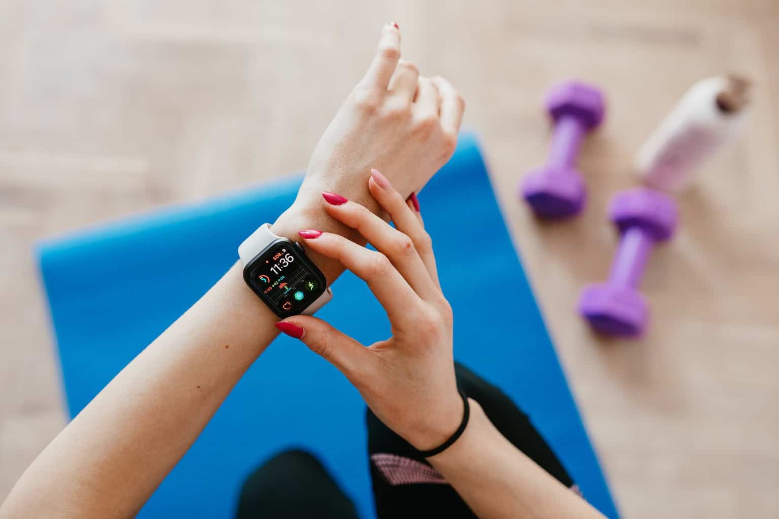 anonymous sportswoman checking smart watch and sitting on mat