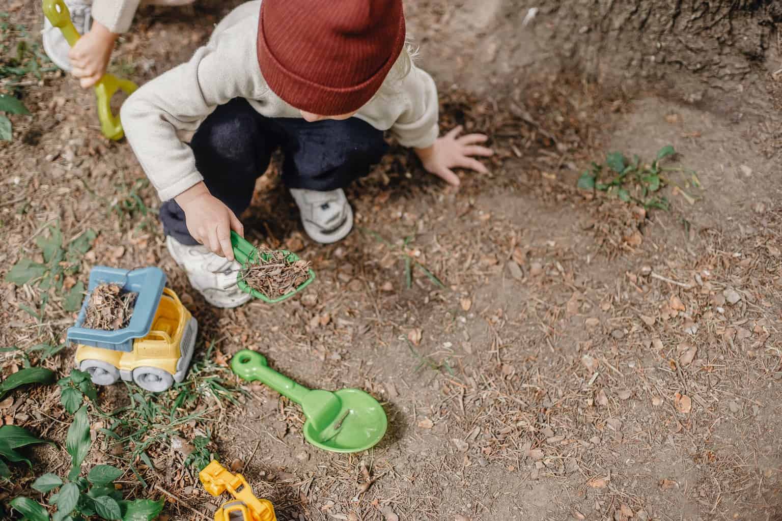 little kid playing with plastic shovel and car in yard