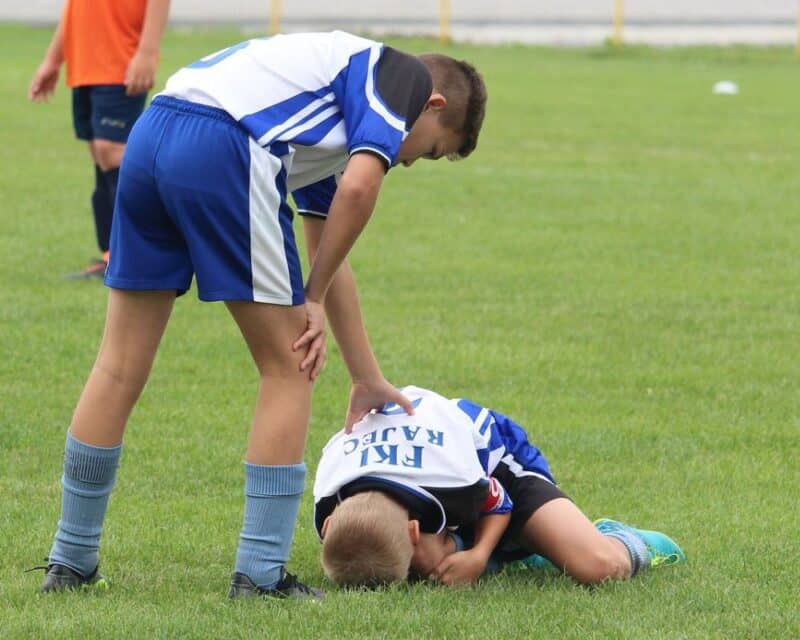 a boy kneeling on the ground with another boy in the back