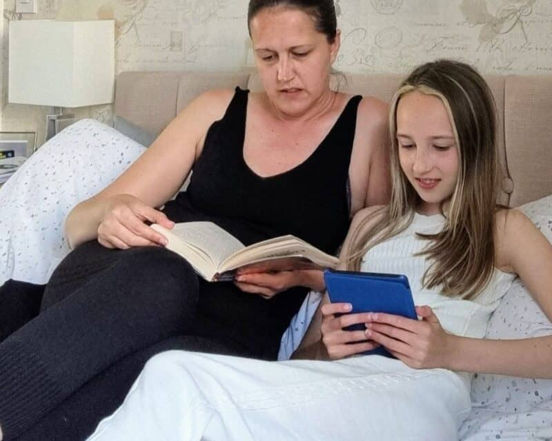 a woman and a girl sitting on a bed reading a book