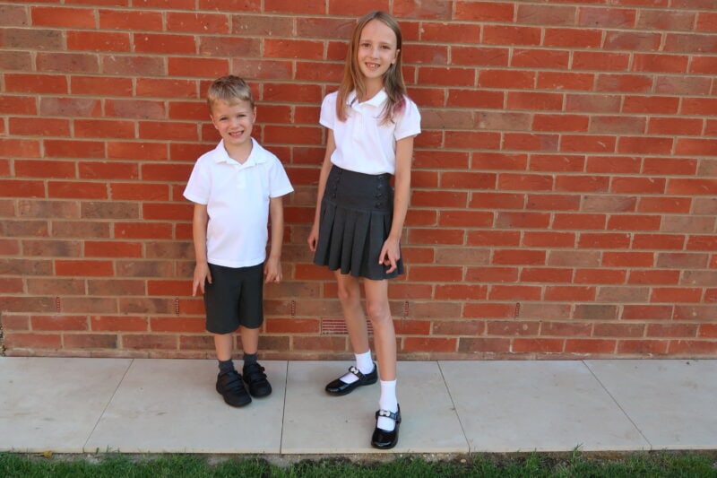 a boy and girl standing in front of a brick wall in school uniform