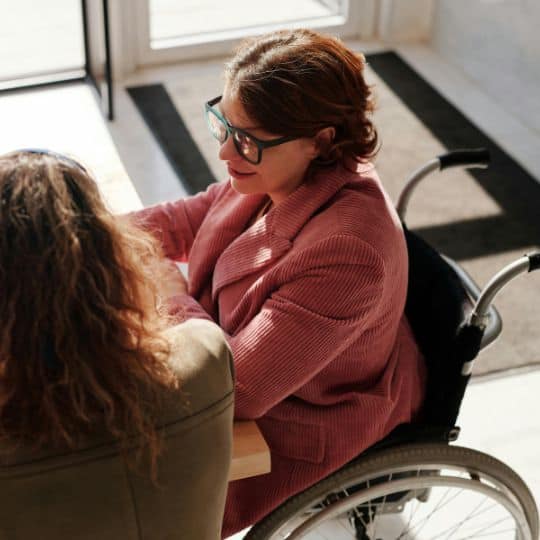a woman in a wheelchair talking to another woman