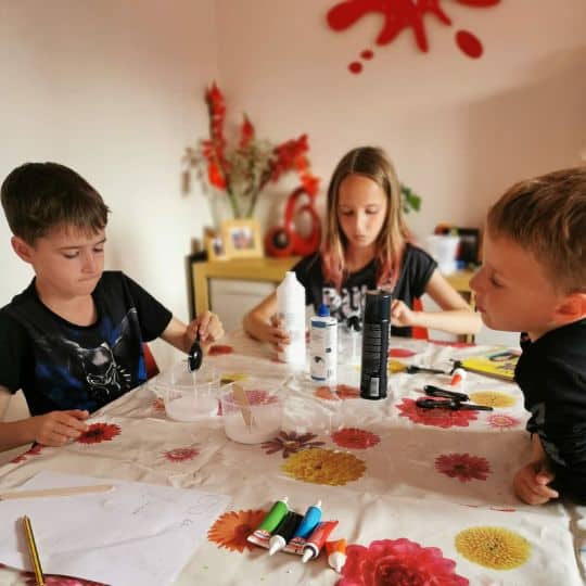 a group of kids sitting at a table with paint cans and glue