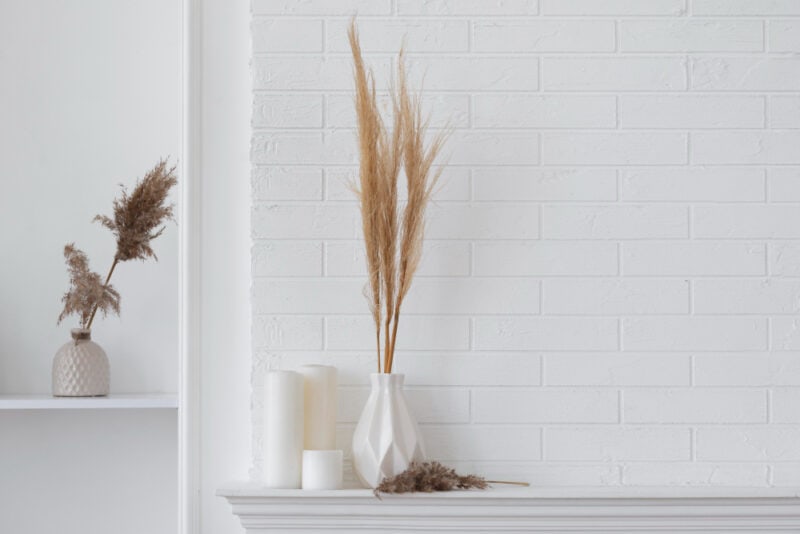 a white vase with dried plants and candles on a white shelf