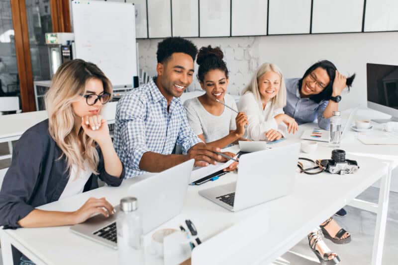 a group of people sitting around a table with laptops