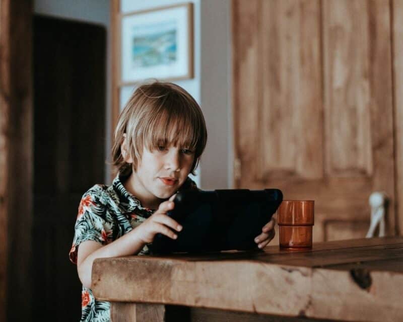 a boy sitting at a table with a tablet